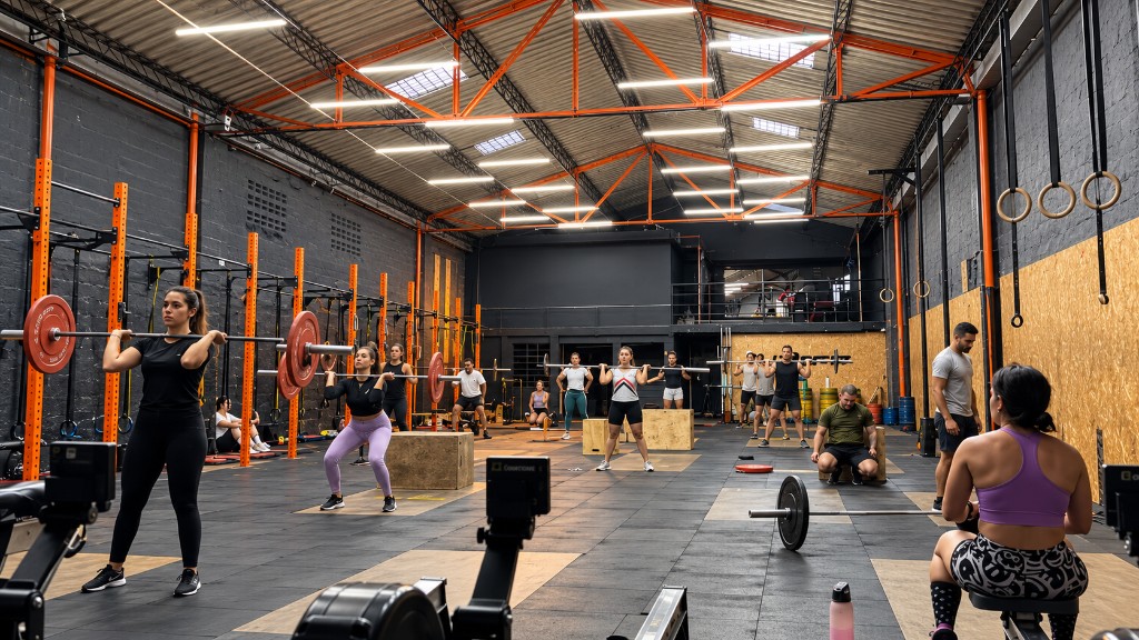 Cours dans une box CrossFit avec des fermes orange : des athlètes aux barres, sur des boxes et sur un rameur.