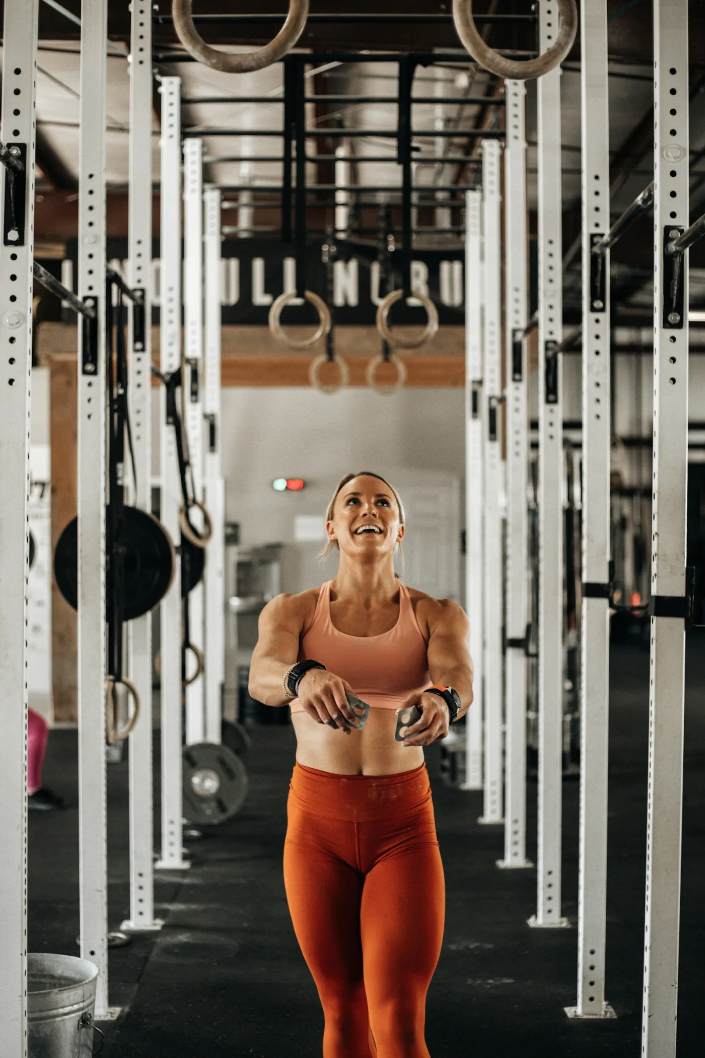 Atleta sorridente in un box CrossFit, con anelli e rack sullo sfondo.