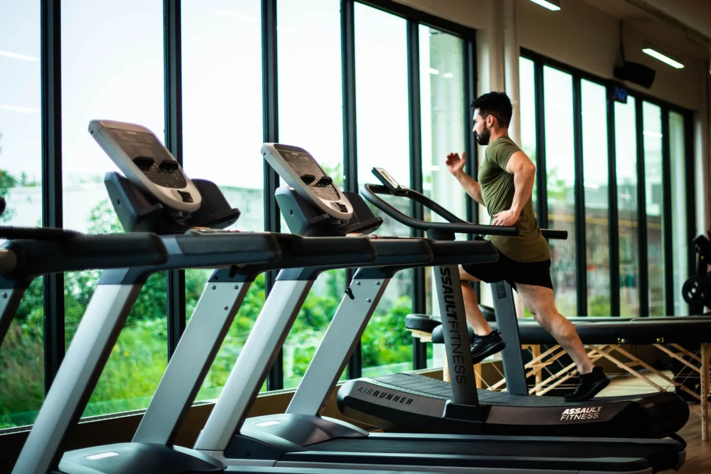 Iscritto che corre sul tapis roulant in una palestra luminosa affacciata sul verde.