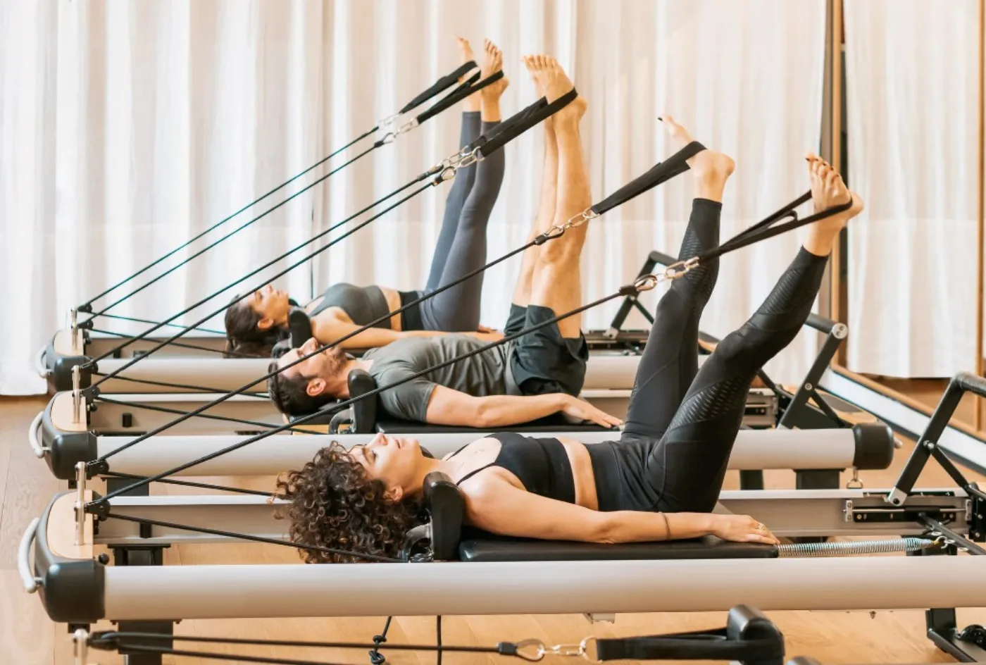Tre allievi su reformer in studio luminoso durante una lezione di gruppo.