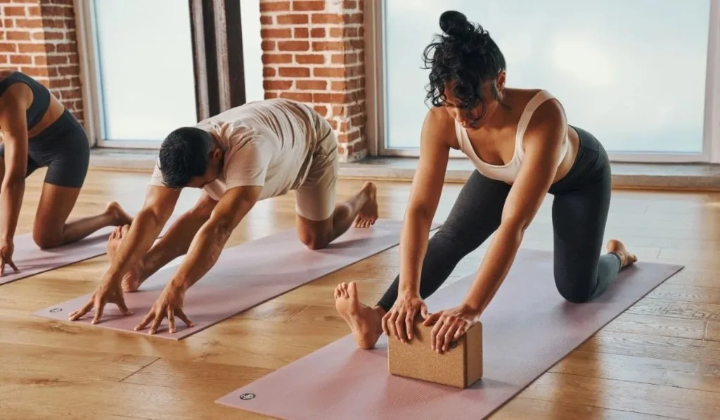 Tre persone in allungamento su tappetini rosa in uno studio yoga luminoso.